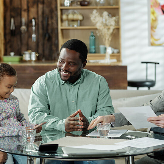 Group of cheerful ethnic couple with daughter and adult bearded agent gathering at table to discuss real estate mortgage