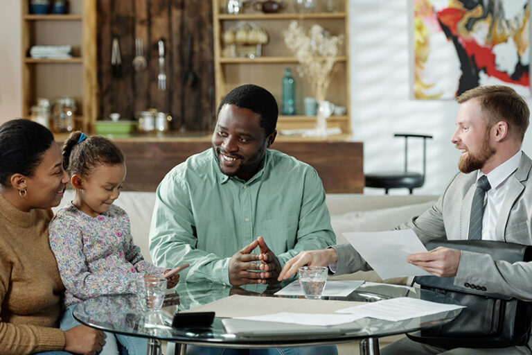 Group of cheerful ethnic couple with daughter and adult bearded agent gathering at table to discuss real estate mortgage