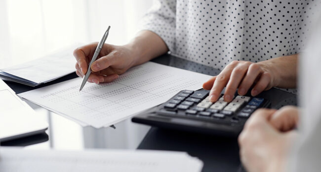 Woman accountant using a calculator and laptop computer while counting taxes for a client. Business audit and finance concepts.