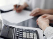 Woman accountant using a pen and laptop computer while counting and discussing taxes with a client, focus on the calculator. Business audit and finance concepts.